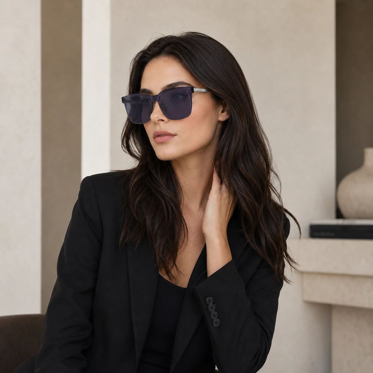 A lifestyle portrait of a woman wearing a black blazer and Baporssa Halo translucent square sunglasses, looking to the side in a minimalist interior setting.