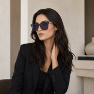 A lifestyle portrait of a woman wearing a black blazer and Baporssa Halo translucent square sunglasses, looking to the side in a minimalist interior setting.