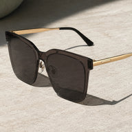 Angled product shot of Baporssa Halo sunglasses on a textured stone surface, highlighting the clear nose pads and the glossy finish of the grey frame.