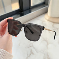 A close-up of a hand holding Baporssa Halo sunglasses, showcasing the translucent grey acetate frame and gold metal hinges.