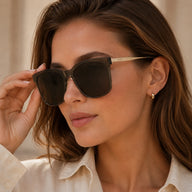 A close-up portrait of a woman adjusting her Baporssa Halo square sunglasses with translucent grey frames and solid dark lenses.