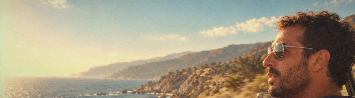A man in BAPORSSA Shift sunglasses driving a convertible along the coast