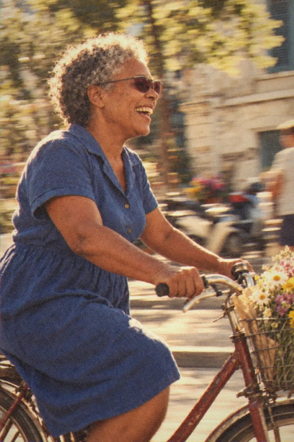 A woman in BAPORSSA Volt claret sunglasses riding a bicycle with a basket of flowers