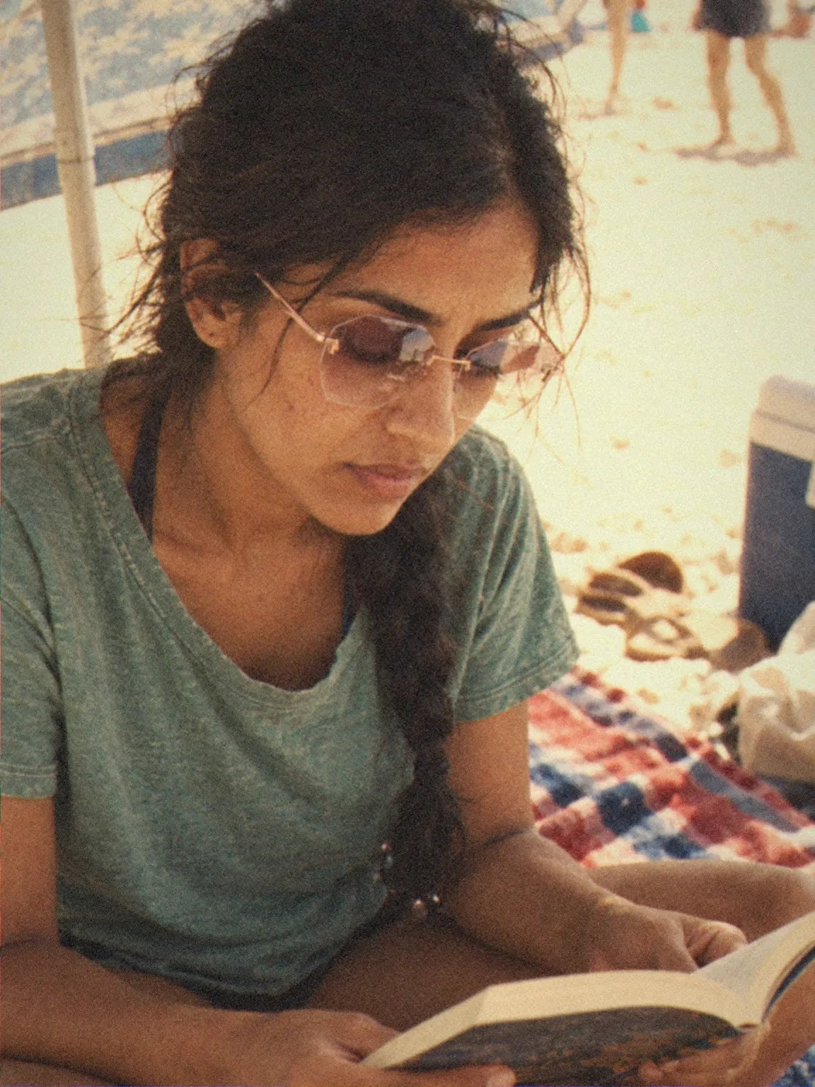 A woman in BAPORSSA Glow rimless sunglasses reading on a beach towel