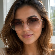 A front-facing close-up portrait of a smiling woman wearing Baporssa rimless sunglasses with brown gradient cut-edge lenses and luxury rose gold hardware.