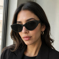 Lyra classic cat-eye sunglasses with thick black frames and solid dark lenses worn by a woman in a black blazer.