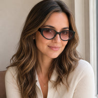 Lyra cat-eye sunglasses with black frame and pink gradient lenses worn by a smiling woman with wavy brown hair.