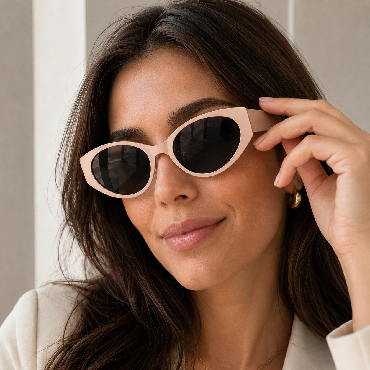 Close-up of a woman adjusting her stylish Lyra nude pink acetate sunglasses with dark-tinted lenses.