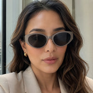 Lyra cat-eye sunglasses with cool stone gray frames and dark solid lenses worn by a woman looking at the camera.