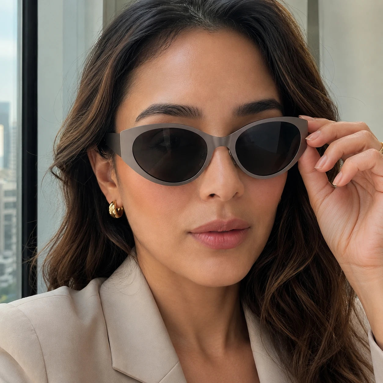 Close-up of a woman adjusting her stylish Lyra cool gray designer sunglasses with dark lenses.