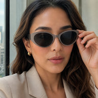 Close-up of a woman adjusting her stylish Lyra cool gray designer sunglasses with dark lenses.