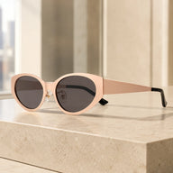 Lyra designer cat-eye sunglasses with nude beige frames and dark lenses on a sunlit marble counter.
