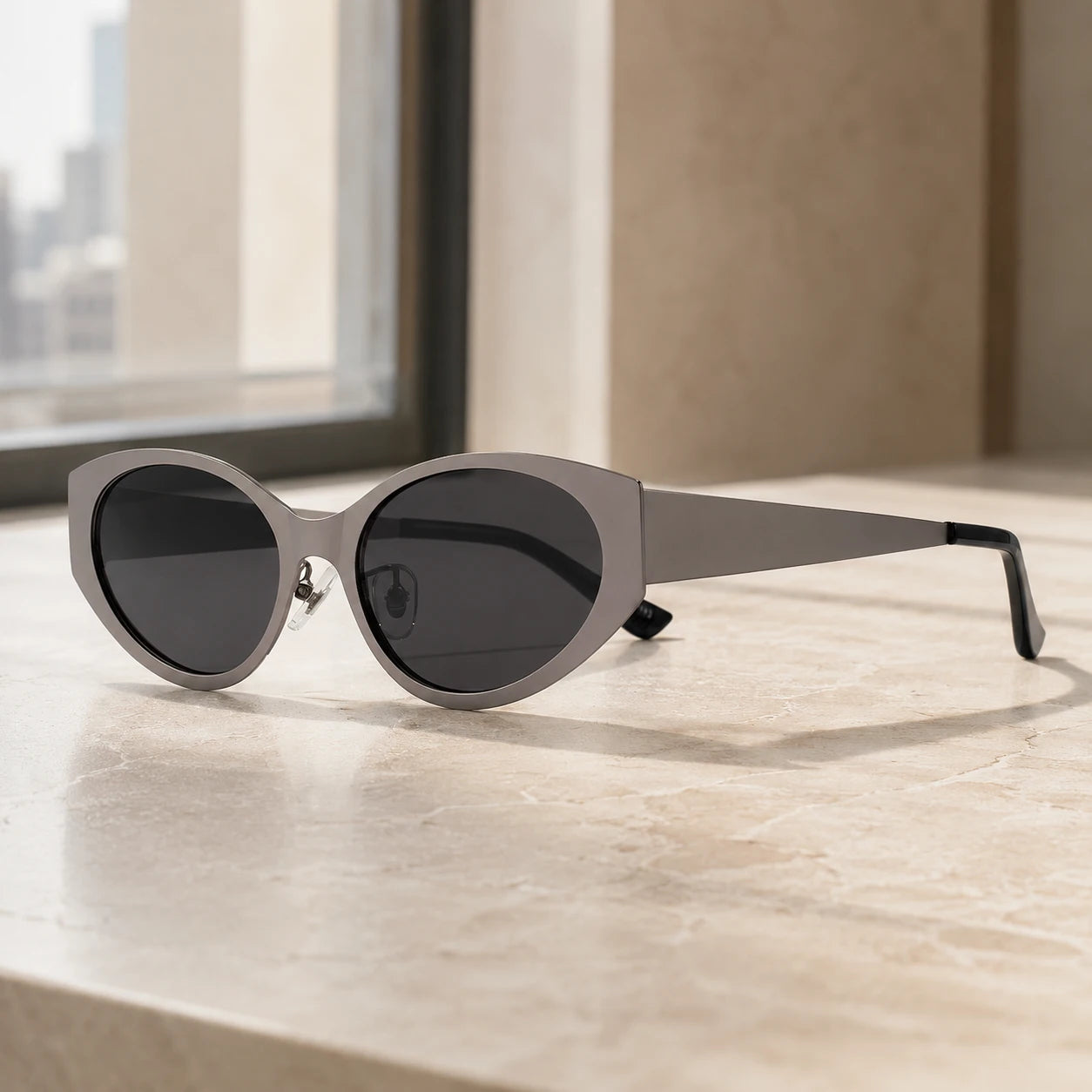 Lyra cool gray cat-eye designer sunglasses displayed on a sunlit beige marble ledge by a window.