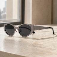 Lyra cool gray cat-eye designer sunglasses displayed on a sunlit beige marble ledge by a window.