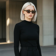 Full-body shot of platinum blonde model in olive green transparent cat-eye sunglasses, black minimalist street style